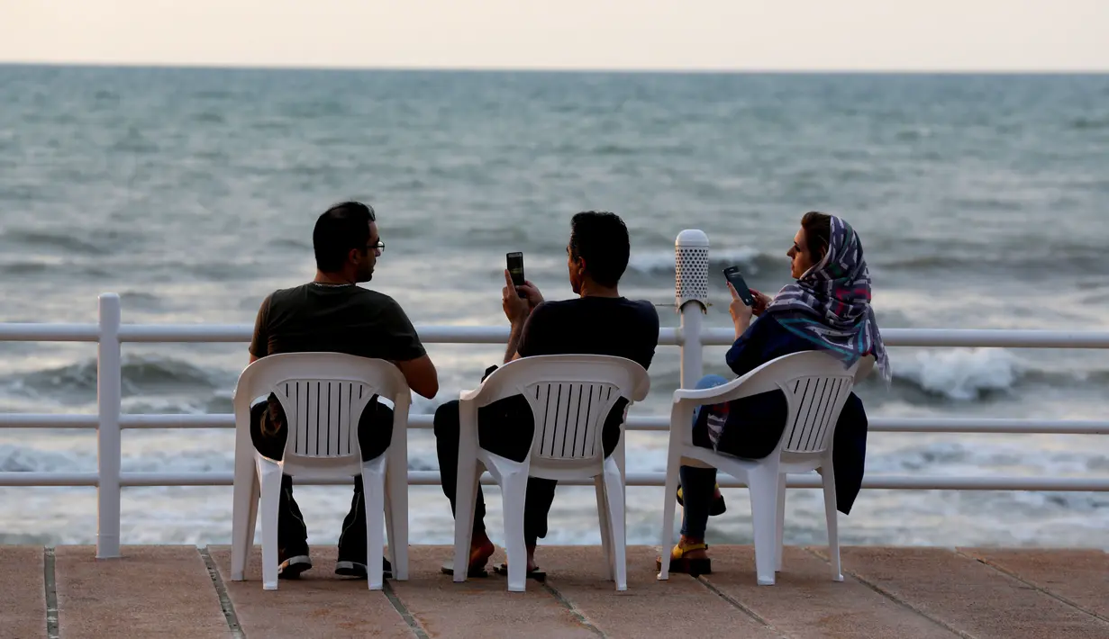 Warga Iran bermain ponsel saat menikmati pantai di kota Laut Kaspia, Izadshahr, di provinsi Mazandaran utara (8/7/2019). Laut Kaspia terletak di antara Eropa dan Asia, di sebelah barat dan barat-daya pegunungan Ural. (AFP Photo/Atta Kenare)