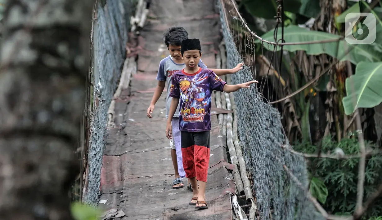 Anak-anak melintasi jembatan gantung yang sudah tidak layak di kawasan Srengseng Sawah, Jakarta, Sabtu (12/6/2021). Jembatan gantung di atas Sungai Ciliwung tersebut saat ini dalam kondisi tidak layak dan dapat membahayakan keselamatan warga yang melintas. (merdeka.com/Iqbal S. Nugroho)