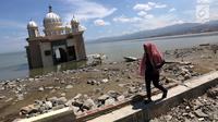 Warga melintas di depan Masjid Terapung Arqam Bab Al Rahman pasca gempa dan tsunami Palu di Pantai Talise, Sulawesi Tengah. Masjid yang dibangun tahun 2011 awalnya menampung 150 jamaah. (Liputan6.com/Fery Padolo)