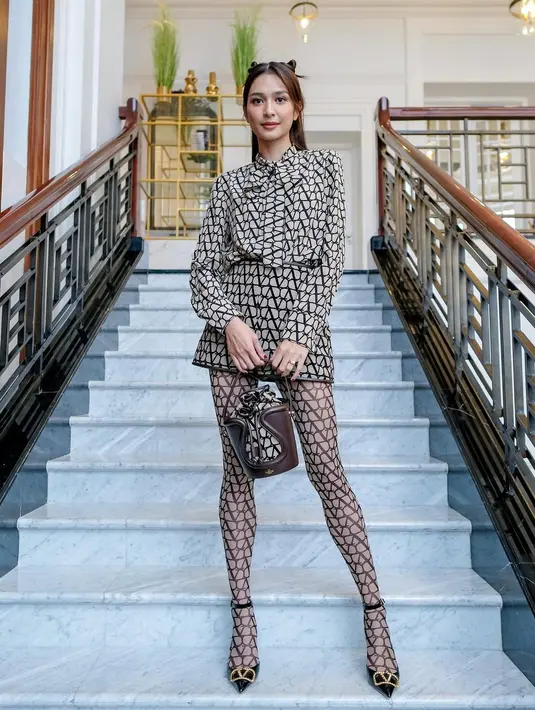 OOTD yang manis dari Mikha Tambayong mengenakan one brand outfit. Ia mengenakan outfit dari Valentino dari atas hingga bawah, atasan lengan panjang berdasi dengan rok mini, dan stoking yang bermotif logo brand, dipadu dengan tas tangan berwarna cokelat yang cantik. [Foto: Instagram/miktambayong]