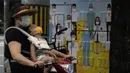 Seorang wanita yang mengenakan masker membawa seorang anak melewati gambar pekerja medis mengenakan masker di Beijing, China, 12 Juli 2022. Beijing telah membatalkan rencana untuk mengizinkan hanya orang yang divaksinasi yang memasuki ruang publik. (AP Photo/Ng Han Guan)