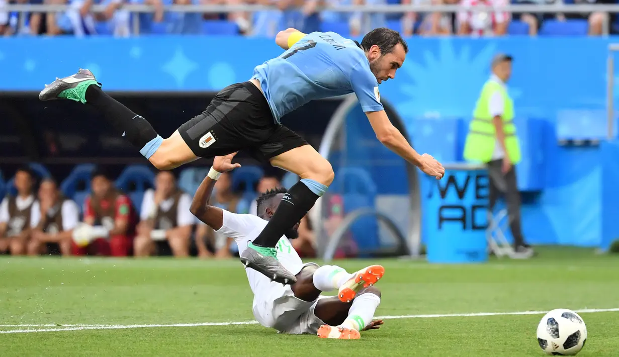 Pemain Arab Saudi, Fahad Al-Muwallad (bawah) menghalau bola dari kejaran pemain Uruguay, Diego Godin pada laga grup A Piala Dunia 2018 di Rostov Arena, Rostov-on-Don, Rusia, (20/6/2018). Uruguay menang 1-0. (AFP/Pascal Guyot)
