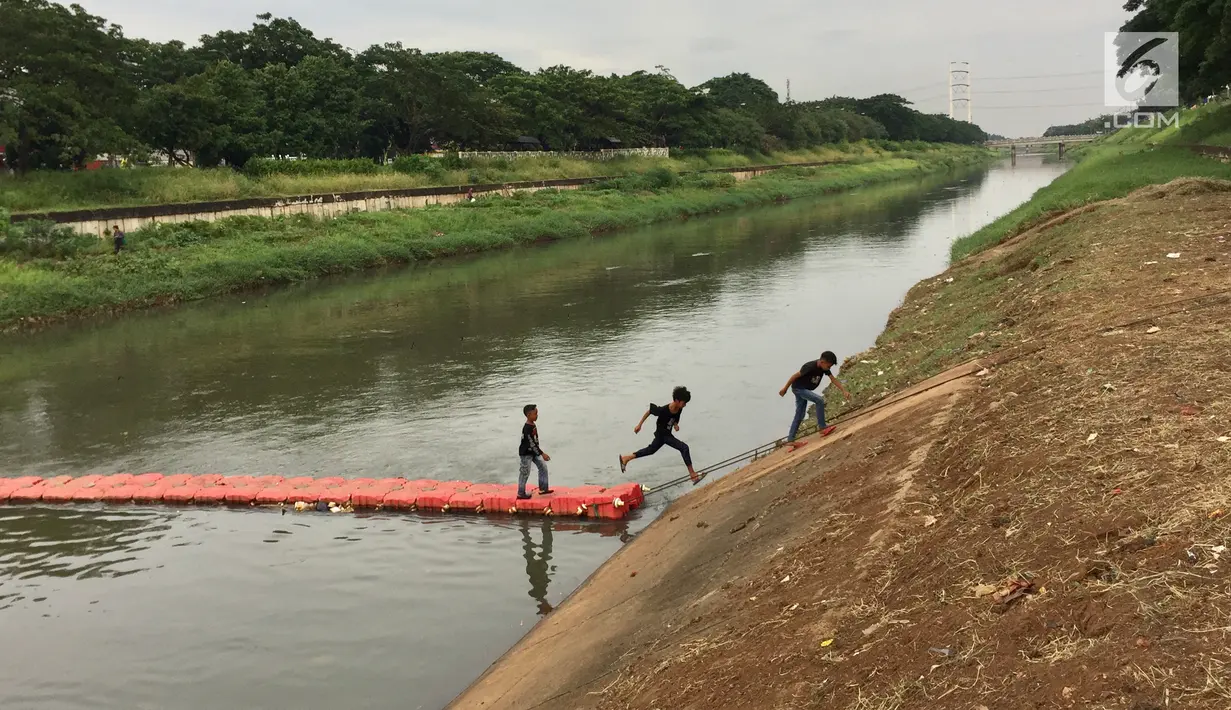 Anak-anak melintasi penyaring sampah untuk menyeberangi Kanal Banjir Timur di Jakarta, Kamis (28/12). Keberadaan penyaring sampah tersebut dimanfaatkan warga sebagai sarana menyeberang untuk mempersingkat waktu tempuh. (Liputan6.com/Immanuel Antonius)