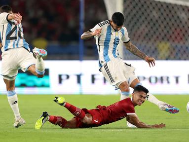 Pemain Timnas Indonesia, Marselino Ferdinan (tengah) terjatuh ketika berebut dengan pemain Argentina, Nahuel Molina (kiri) dan Cristian Romero pada laga FIFA Matchday di Stadion Utama Gelora Bung Karno (SUGBK), Senayan, Jakarta, Senin (19/06/2023). (Bola.com/Bagaskara Lazuardi)