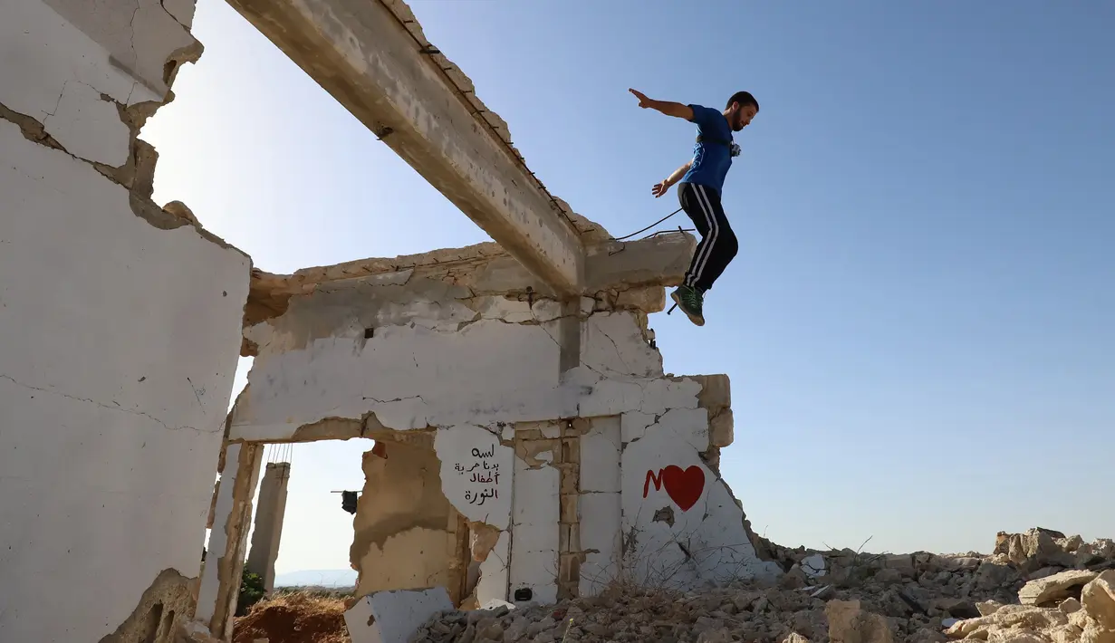 Seorang pemuda Suriah melakukan parkour di atas reruntuhan bangunan yang hancur akibat serangan pasukan rezim di kota Binnish di provinsi barat laut Idlib pada 17 Juni 2020. Parkour merupakan olahraga ketangkasan yang terdiri dari lari, melompat, salto dan berayun. (Abdulaziz KETAZ / AFP)