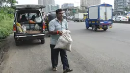 Dadarao Bilhore (48) membawa karung berisi pasir dan kerikil untuk menambal jalan berlubang di kota Mumbai, 29 Agustus 2018. Pedagang sayuran itu melakukan aksi menambal jalanan ini sebagai cara mengingat putra tercintanya. (INDRANIL MUKHERJEE/AFP)