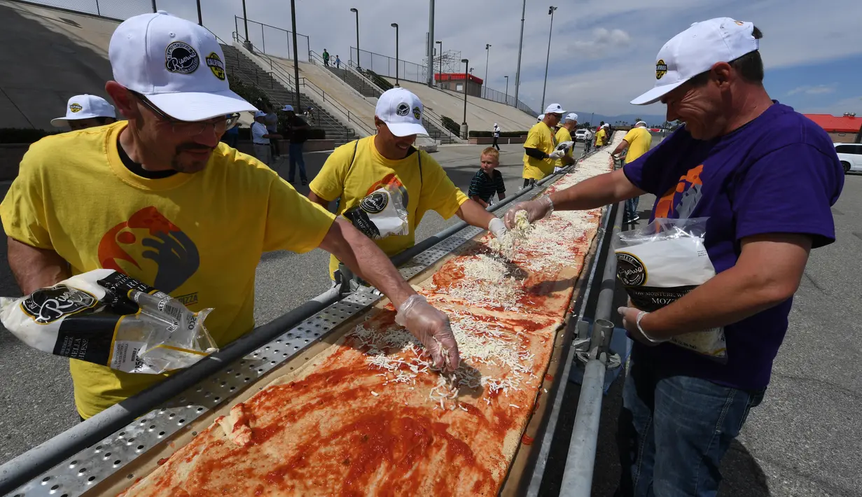 Sejumlah peserta menaburi keju saat membuat pizza panjang di jalur Auto Club Speedway, di Fontana, California (10/6). Rekor baru ini mengalahkan rekor sebelumnya yang dipegang oleh peserta di Italia dengan pizza sepanjang 1,8 km. (AFP/Mark Ralston)