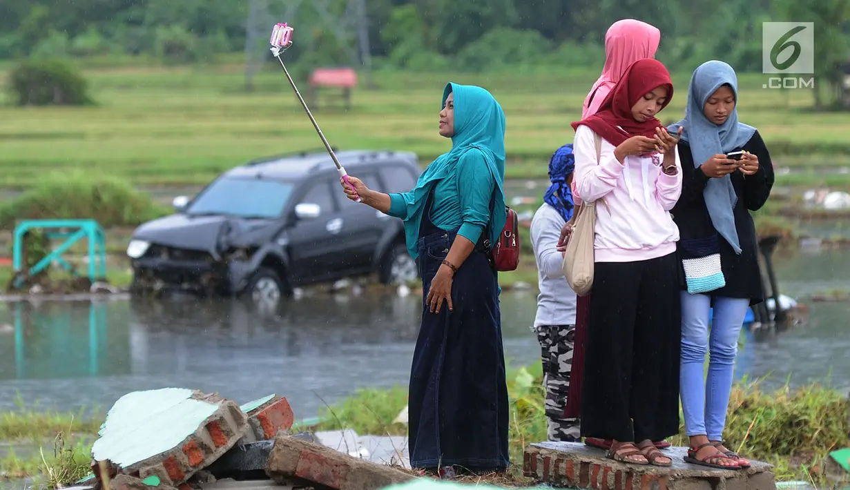 Warga berselfie dengan latar belakang kawasan terdampak bencana tsunami di Carita, Banten, Selasa (25/12). Libur Natal dimanfaatkan warga luar Anyer dan carita untuk menyaksikan langsung terdampak bencana sambil berselfie. (Merdeka.com/Arie Basuki)