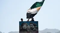 Warga mengibarkan bendera di atas potret mendiang komandan Afghanistan Ahmad Shah Massoud (kanan) di Distrik Paryan, Provinsi Panjshir, Afghanistan, 23 Agustus 2021. Taliban berusaha untuk bernegosiasi daripada melawan kelompok perlawanan di Lembah Panjshir. (Ahmad SAHEL ARMAN/AFP)