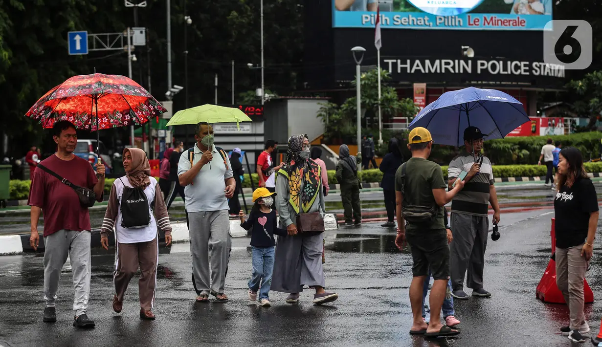 Warga dengan menggunakan payung beraktivitas di tengah rintik hujan pada Car Free Day atau hari bebas kendaraan di kawasan Bundaran Hotel Indonesia (HI), Jakarta, Minggu (12/2/2023). Hujan yang mengguyur Ibu Kota sejak malam sampai pagi ini tak menyurutkan semangat warga untuk tetap berolahraga di area CFD. (Liputan6.com/Johan Tallo)