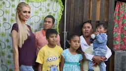 Paris Hilton foto bersama dengan salah satu keluarga terkena dampak gempa bumi pada September 2017 di San Gregorio Atlapulco, Meksiko (12/11). Paris Hilton tampil mengenakan kaos, jeans dan sepatu hitam. (AFP Photo/Antonio Nava)