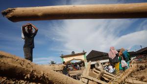 Selain rumah warga terdampak, kayu-kayu gelondongan juga masih terlihat tertumpuk di sepanjang aliran Sungai Aek Garoga dan Sungai Batang Toru. Tampak dalam foto, para penyintas berjalan melewati tumpukan kayu yang tersapu banjir bandang di Batang Toru, Sumatra Utara, Selasa 2 Desember 2025. (AP Photo/Binsar Bakkara)