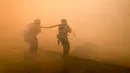 Dua petugas pemadam kebakaran berusaha memadamkan api di sepanjang Ronald Reagan (118) Jalan Bebas Hambatan di Simi Valley, Californnia (12/11). Kebakaran yang terjadi dilaporkan telah menewaskan puluhan orang. (AP Photo / Ringo H.W. Chiu)