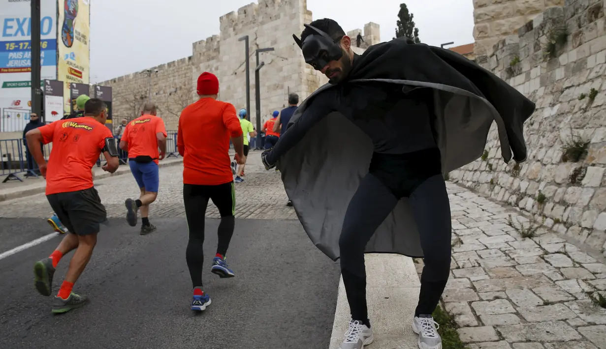 Seorang pria mengenakan kostum superhero Batman menggoda para atlet lari di kota tua, Yerusalem, Israel, (18/2).  Sejumlah orang mengikuti lomba lari Maraton Internasional  yang ke-6 di Yerusalem. (REUTERS / Baz Ratner)