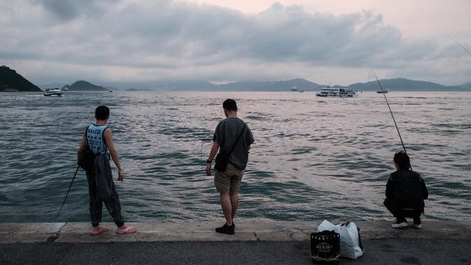 Sejumlah pria memancing dari dermaga di Victoria Harbour di Hong Kong (21/4/2020). Kepala eksekutif Carrie Lam mengatakan langkah-langkah jarak sosial dan beberapa pembatasan bisnis akan berlanjut selama dua minggu hingga setidaknya 7 Mei. (AFP/Anthony Wallace)