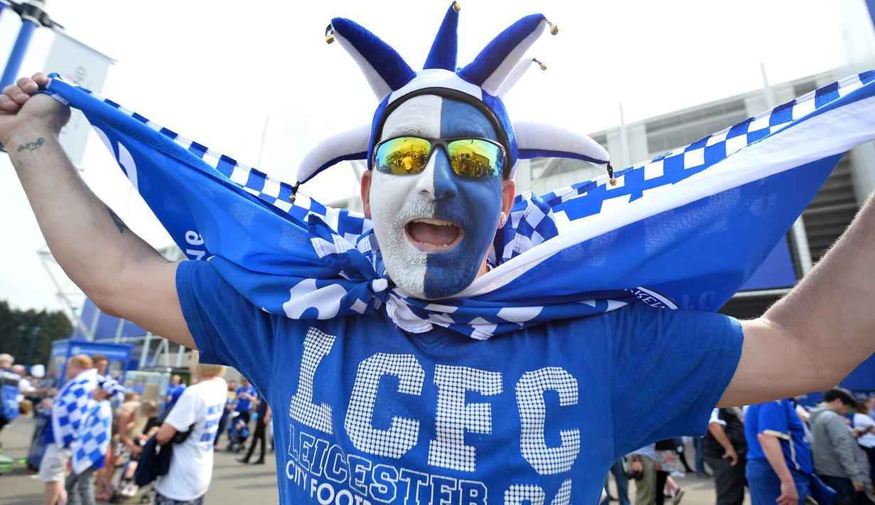 Seorang suporter mengenakan topi ala badut dan wajah yang dicat dengan warna kebanggan Leicester City memeriahkan  perayaan titel juara Liga Inggris di Stadion King Power, (7/5/2016). (AFP/Glyn Kirk)