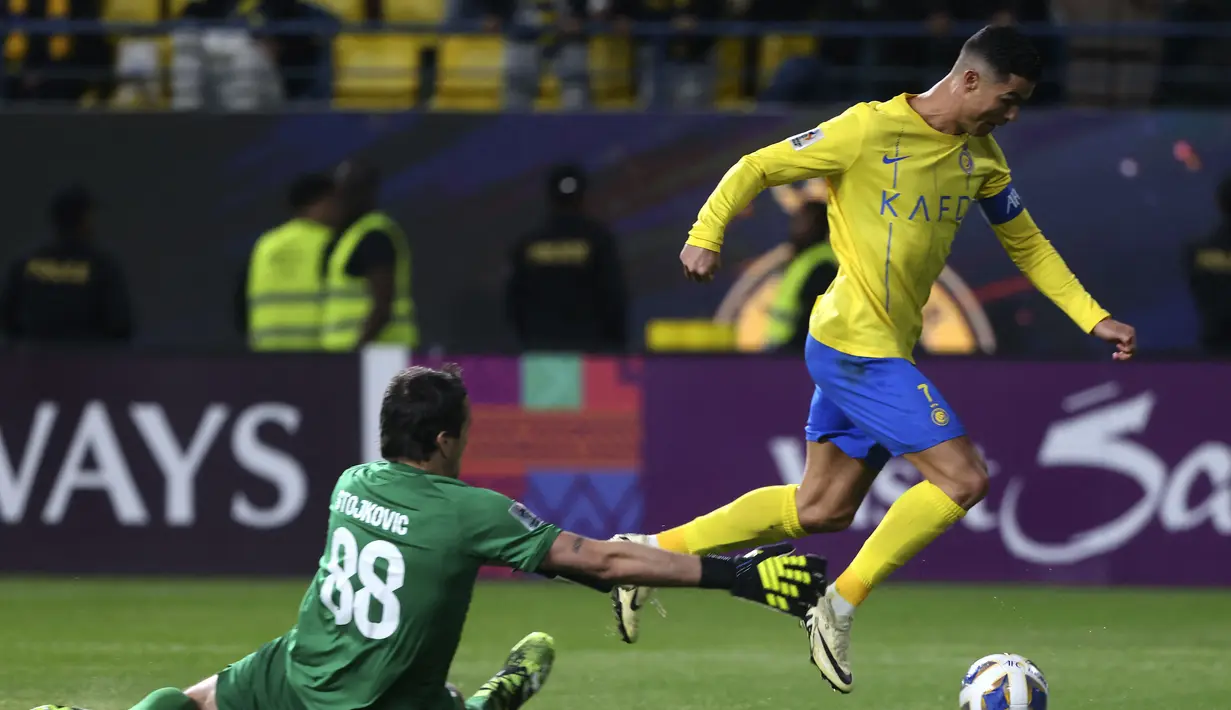 Pemain Al-Nassr, Cristiano Ronaldo berusaha mencetak gol dengan melewati kiper Al-Fieha, Vladimir Stojkovic saat laga 16 besar Liga Champions Asia 2023/2024 di Al-Awwal Park Stadium, Riyadh, Arab Saudi Rabu (21/02/2024) waktu setempat. (AFP/Fayez Nureldine)