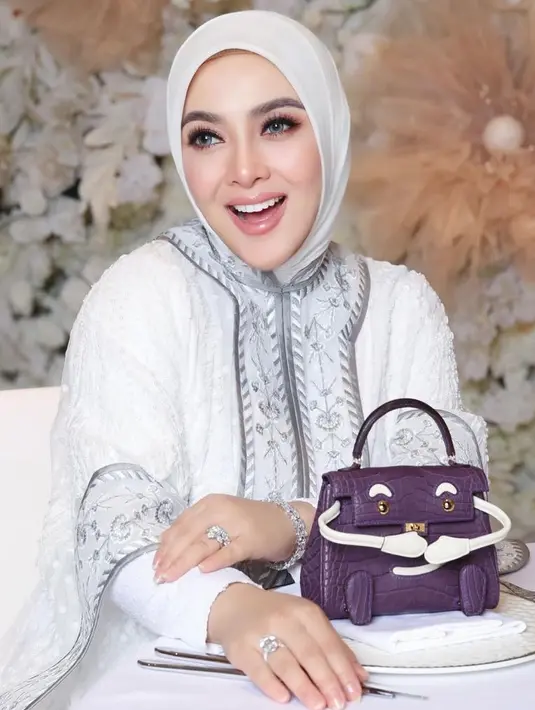 Saat syukuran, Syahrini mengenakan dress putih senada dengan outer dan kerudungnya. Ia juga membawa tas Hermes ungu model kelly doll matte alligator nya. [@princessyahrini]
