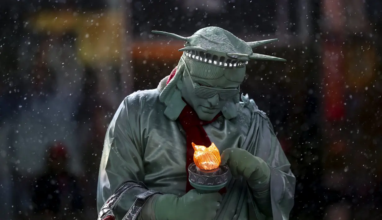 Seorang pria berpakaian seperti "Patung Liberty" memperbaiki lampu yang dipegangnya saat salju turun di Times Square di Manhattan borough New York, (22/1/2016). (REUTERS/Carlo Allegri)