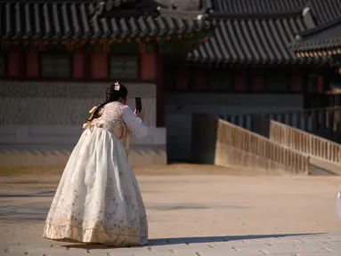 Pengunjung mengenakan pakaian tradisional Hanbok mengambil foto di istana Changdeokgung di Seoul , Korea Selatan (2/4). Korea Selatan sedang bersiap untuk meluncurkan jaringan seluler 5G pertama di dunia pada 5 April. (AFP Photo/Ed Jones)