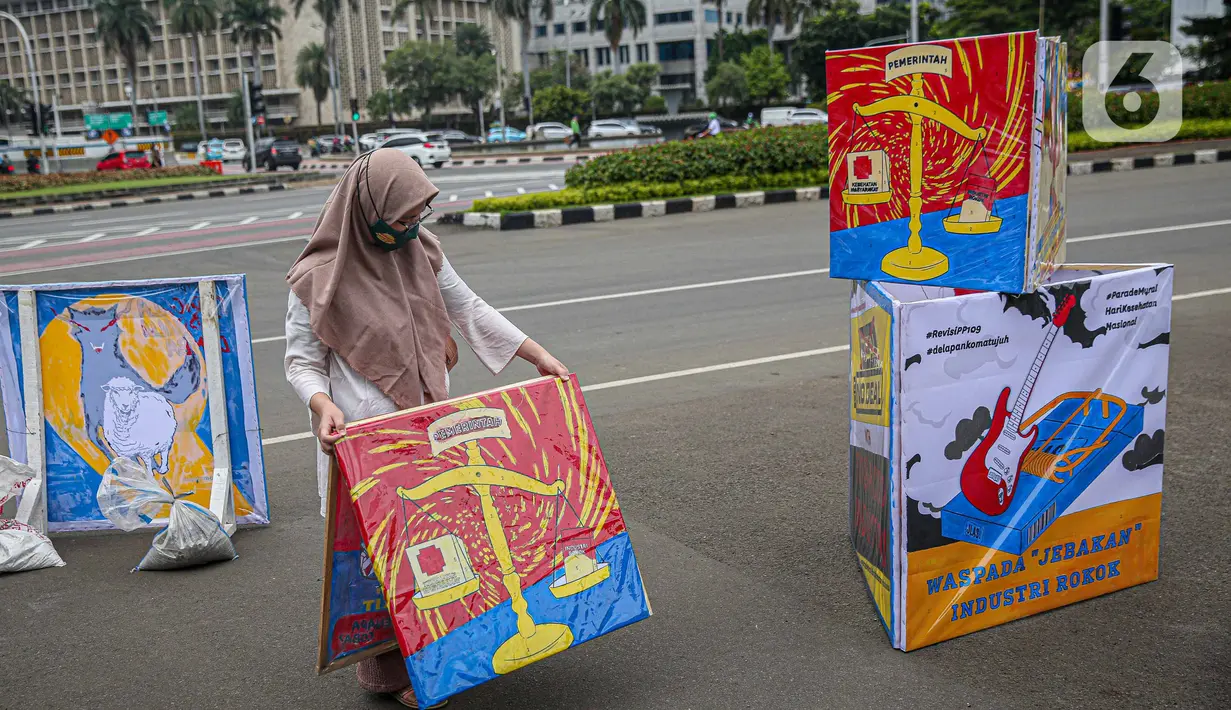 Seorang yang tergabung dalam Koalisi Masyarakat Peduli Kesehatan (KOMPAK) menunjukkan poster saat menggelar aksi #ParadeMural di kawasan Patung Arjuna Wijaya, Jakarta, Rabu (17/11/2021). Aksi juga dilakukan untuk menyambut Hari Kesehatan Nasional 2021. (Liputan6.com/Faizal Fanani)