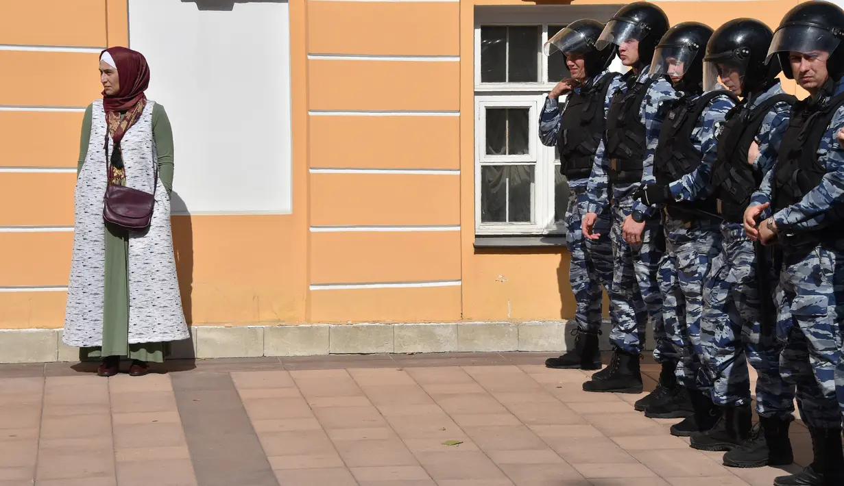 Seorang wanita muslim berdiri dekat polisi anti huru-hara yang berjaga saat unjuk rasa di depan Kedubes Myanmar di pusat kota Moskow, Rusia, Minggu (3/9). Ratusan muslim berkumpul dan melakukan aksi solidaritas bagi Muslim Rohingya. (Vasily MAXIMOV/AFP)