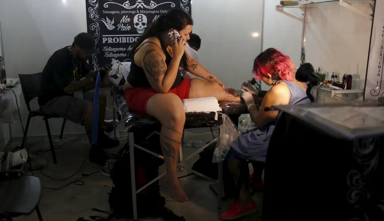 Seorang seniman terlihat serius menato seorang wanita dibagian kakinya saat Festival Internasional Tattoo Week Rio 2016 ketiga di Rio de Janeiro, Brasil, (22/1/2016). (REUTERS/Pilar Olivares)