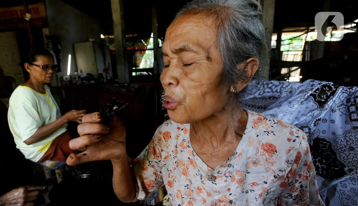 Perajin meniup canting atau alat yang digunakan untuk membatik saat menyelesaikan pembuatan batik tulis di Tie Poek Batik, Trenggalek, Jawa Timur, Sabtu (2/9/2023). (merdeka.com/Arie Basuki)