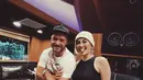 Agnez Mo juga tampil dengan tank top hitam yang memerlihatkan otot perutnya. Atasan dipadukan celana denim dan beanie hat putih. (@agnezmo)