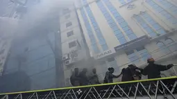 Petugas pemadam kebakaran Bangladesh menuntun orang menuruni tangga di bawah gedung kantor yang terbakar di Dhaka (28/3). Kebakaran besar melanda gedung perkantoran yang menewaskan sedikitnya lima orang dan lainnya masih terperangkap dalam gedung yang terbakar tersebut. (AFP/Munir Uzzaman)