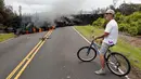 Seorang warga berfoto dengan latar belakang lava pijar erupsi Gunung Kilauea yang menutupi jalan di Pahoa, Hawaii, Amerika Serikat, Sabtu (5/5). Menurut warga, aliran lava tersebar di area seluas 200 yard atau 182 meter persegi. (AP Photo/Marco Garcia)