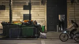 Seorang pria mengendarai sepeda melewati tong sampah yang tidak diambil di pintu masuk staf Istana Elysee di Paris, Prancis, Senin (13/3/2023). Selain sampah yang menumpuk di jalanan, aksi mogok kerja besar-besaran ini menganggu layanan kereta api, memicu sekolah-sekolah diliburkan, dan menghentikan pengiriman bahan bakar. (AP Photo/Michel Euler)