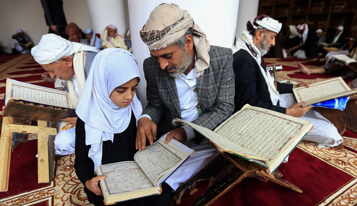 Seorang pria membaca Al-Quran bersama putrinya selama bulan Ramadan di Masjid Agung Sanaa, Yaman, Minggu (26/4/2020). Masjid Agung Sanaa bagian dari Situs Warisan Dunia UNESCO. (Mohammed HUWAIS/AFP)