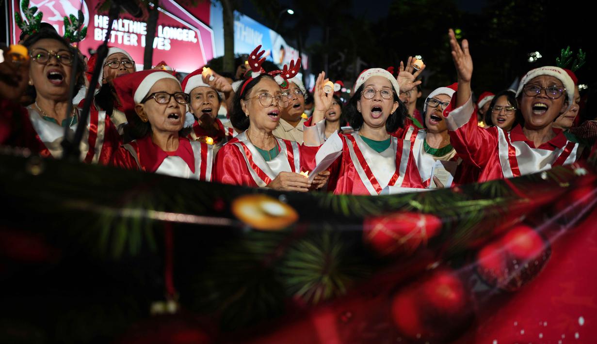 Beberapa di antaranya ada yang mengenakan topi Santa, tanduk rusa, hingga lampu hias di kepala. Tampak dalam foto, Umat Kristiani menyanyikan lagu-lagu Natal di Jakarta, Indonesia, Selasa, 23 Desember 2025. (AP Photo/Dita Alangkara)