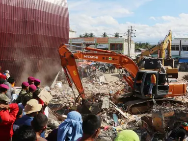 Eskavator membantu mengangkat puing bangunan yang runtuh akibat gempa di Pasar Meureudu, Pidie Jaya, Aceh, Kamis (8/12). Dikabarkan korban meninggal sudah mencapai 102 orang. (Liputan6.com/Angga Yuniar)