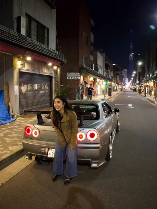 Dalam salah satu potret malam hari, Febby tampil santai mengenakan jaket olive dipadukan wide leg jeans dan pointed boots hitam. Pose candid di depan mobil sport bernuansa vintage membuat fotonya terasa cinematic khas film Jepang. [@febbyrastanty].