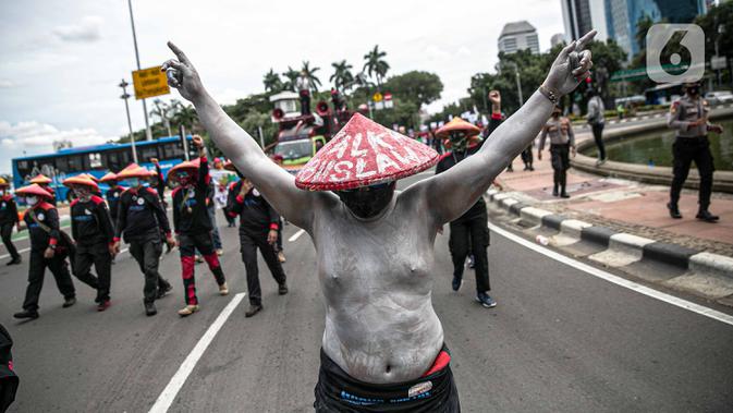 Seorang buruh dengan tubuh di cat silver berunjuk rasa menyuarakan penolakan kaum buruh terhadap omnibus law UU Cipta Kerja di kawasan Patung Kuda, Jakarta, Rabu (16/12/2020). Unjuk rasa ini dihadiri ratusan buruh. (Liputan6.com/Faizal Fanani)