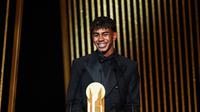 Penyerang muda Barcelona, Lamine Yamal, menerima Kopa Trophy, lambang pemenang predikat pemain muda terbaik di seremonial Ballon d'Or yang berlangsung di Theatre du Chatelet di Paris, Senin (28/10/2024) malam waktu setempat. (FRANCK FIFE / AFP)