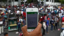 Pendemo menunjukkan aplikasi transportasi online saat unjuk rasa di Makassar, Rabu (1/11). Mereka menggeruduk kantor Gubernur Sulsel untuk menuntut maraknya transportasi online yang dianggap memakan rezeki mereka. (AFP Photo/Yusuf Wahil)