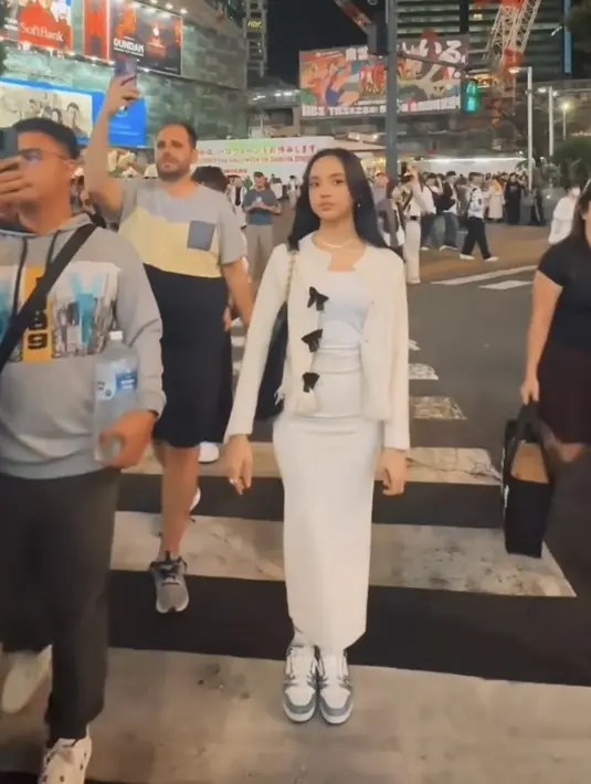 Lyodra tampil serba putih dengan mengenakan spaghetti strap inner, dipadukan cardigan berpita hitam dan long skirtnya. Serta sneakes nya, tas Chanel hitam melengkapi tampilannya. [@lyodraofficial]