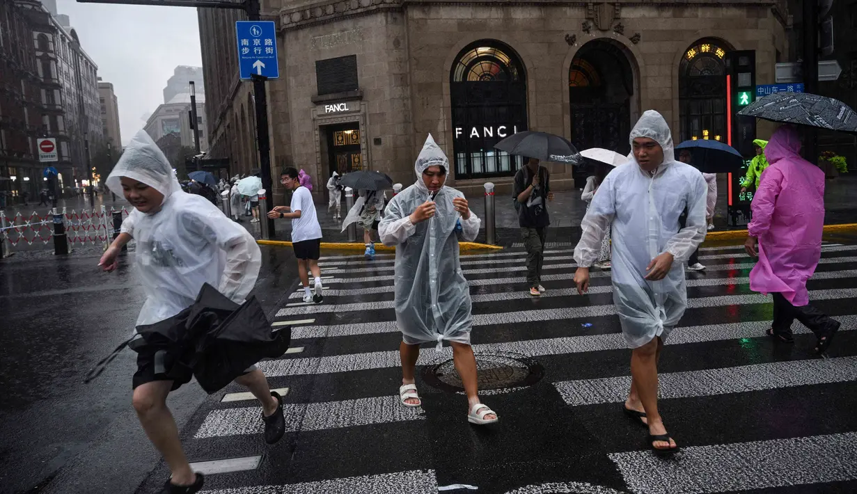 Orang-orang melindungi diri mereka dengan mantel hujan sekali pakai selama perjalanan Topan Co-May di Shanghai pada tanggal 30 Juli 2025. (Hector RETAMAL/AFP)