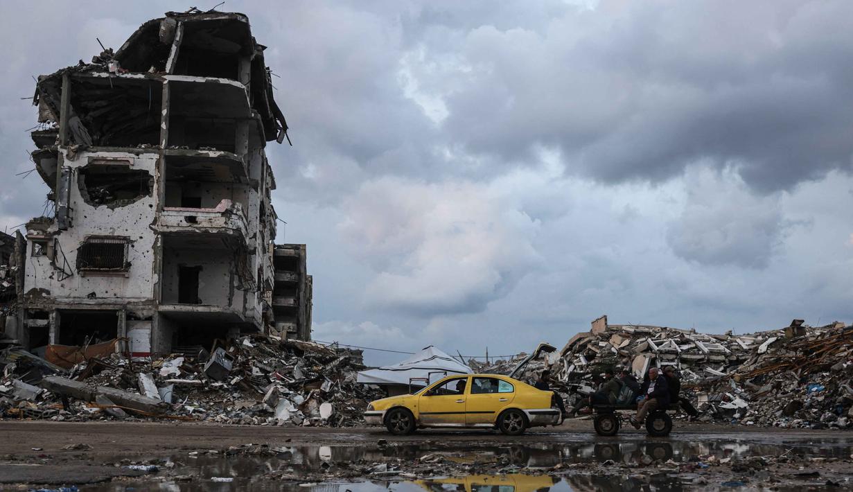 Di sisi lain, Perserikatan Bangsa Bangsa (PBB) memperkirakan, sejak konflik antara Israel dan Hamas dimulai pada Oktober 2023 lalu, sekitar 92 persen dari seluruh bangunan tempat tinggal di Gaza telah rusak atau hancur. Tampak dalam foto, seorang pria mengendarai mobil kuning di samping genangan air di lingkungan Al-Saftawi, sebelah barat kota Jabalia di Jalur Gaza utara pada Rabu 10 Desember 2025. (BASHAR TALEB/AFP)