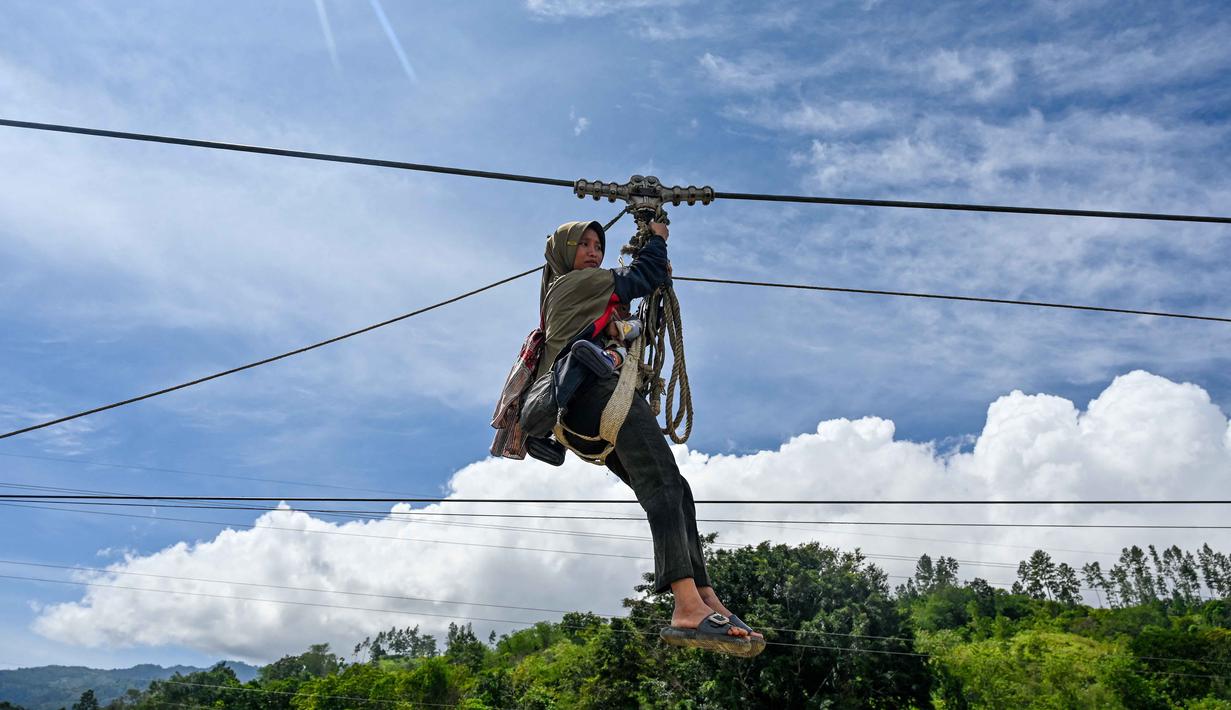 Seorang wanita dan bayinya menggunakan tali untuk menyeberangi sungai setelah banjir bandang yang menghancurkan desa-desa di sekitarnya di Ketol, provinsi Aceh, pada Selasa 6 Januari 2026. Lebih dari satu bulan setelah banjir bandang dan tanah longsor melanda sejumlah desa di Kecamatan Ketol, Aceh Tengah. (CHAIDEER MAHYUDDIN/AFP)