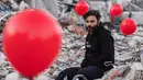 Ogun Sever Okur, pria Turki berusia 38 tahun berpose di antara balon yang tergantung di puing-puing bangunan yang runtuh di Antakya, Turki selatan pada 21 Februari 2023, menyusul gempa berkekuatan 6,4 yang melanda pada 20 Februari, dua minggu setelah gempa berkekuatan 7,8 -gempa berkekuatan melanda dekat Gaziantep dan telah menewaskan lebih dari 44.000 orang.