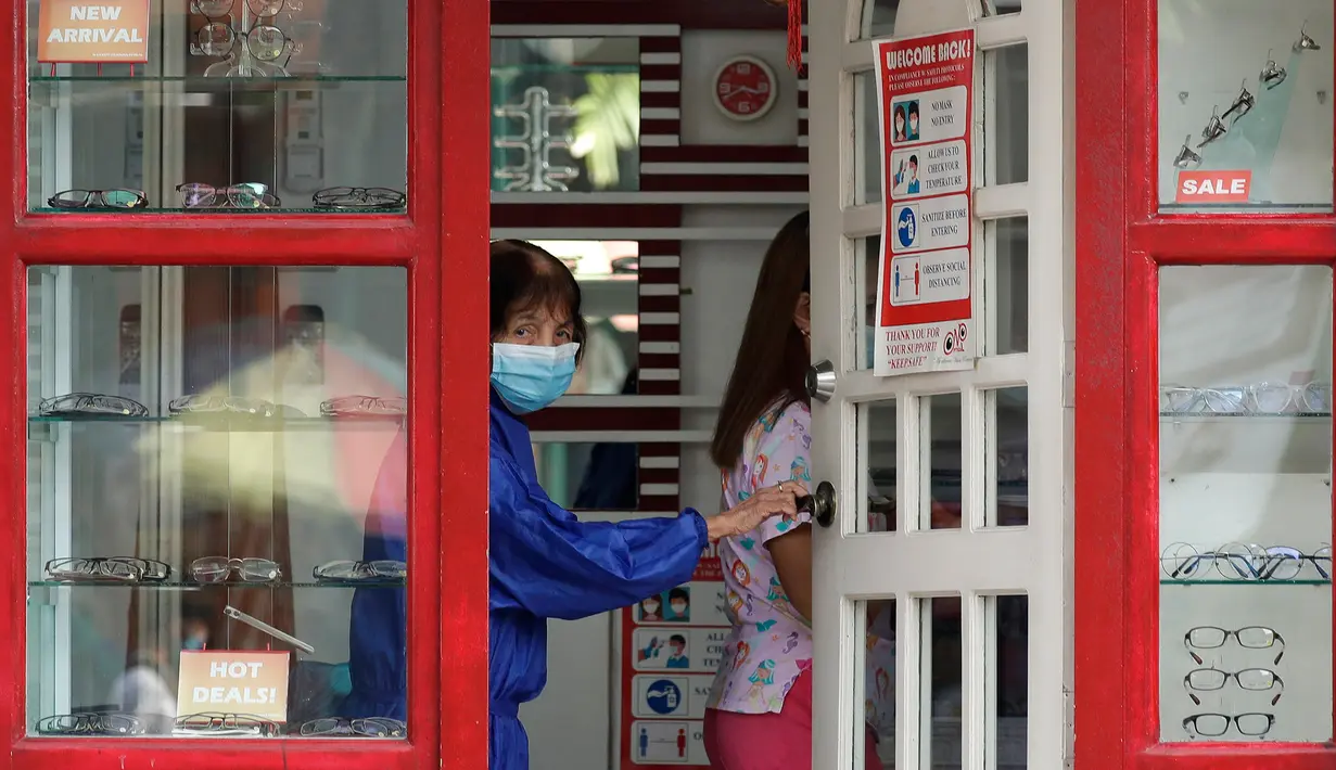 Seorang perempuan yang mengenakan masker membuka pintu toko optik di kota Quezon, Filipina, Selasa (22/9/2020). Presiden Filipina Rodrigo Duterte mengatakan telah memperpanjang status masa darurat virus corona (Covid-19) di negaranya hingga satu tahun ke depan. (AP Photo/Aaron Favila)