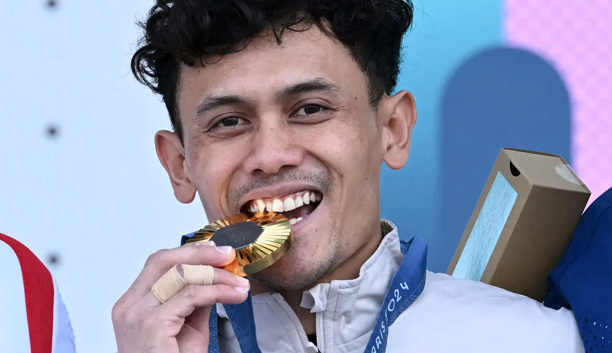 <p>Atlet panjat tebing Indonesia, Veddriq Leonardo menggigit medali emas saat di atas podium cabang olahraga panjat tebing nomor speed Olimpiade Paris 2024 di Le Bourget Sport Climbing Venue, Paris, Prancis, Kamis (08/08/2024). (AFP/Jonathan Nackstrand)</p>