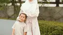 Larissa Chou tampil dengan gamis warna pastel dipadukan kerudung putih, sedangkan si kecil mengenakan baju koko dipadukan celana hitamnya. [@larissachou]