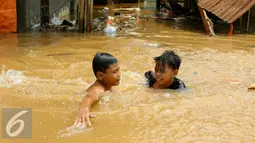 Anak-anak bermain di lokasi banjir yang merendam kawasan Kampung Pulo, Jakarta, Rabu (25/11). Air aliran kali Ciliwung mulai memasuki rumah warga sekitar pukul 03.00 Wib dini hari tadi. (Liputan6.com/Yoppy Renato)