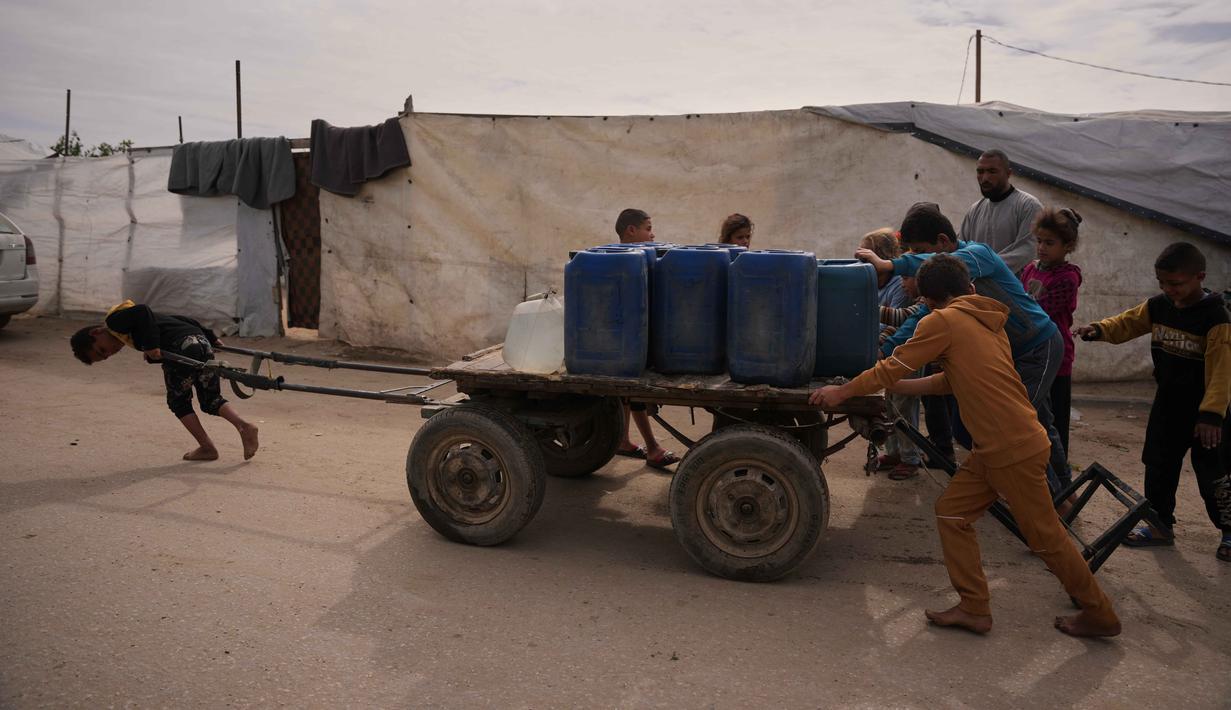 Mayoritas warga Palestina di Gaza masih sangat bergantung pada bantuan kemanusiaan yang masuk secara terbatas dan sering terhambat oleh kebijakan blokade. Tampak dalam foto, anak-anak Palestina mendorong gerobak yang berisi wadah plastik berisi air yang dikumpulkan dari pabrik desalinasi, Khan Younis, Jalur Gaza selatan, Jumat 6 Februari 2026. (AP Photo/Abdel Kareem Hana)