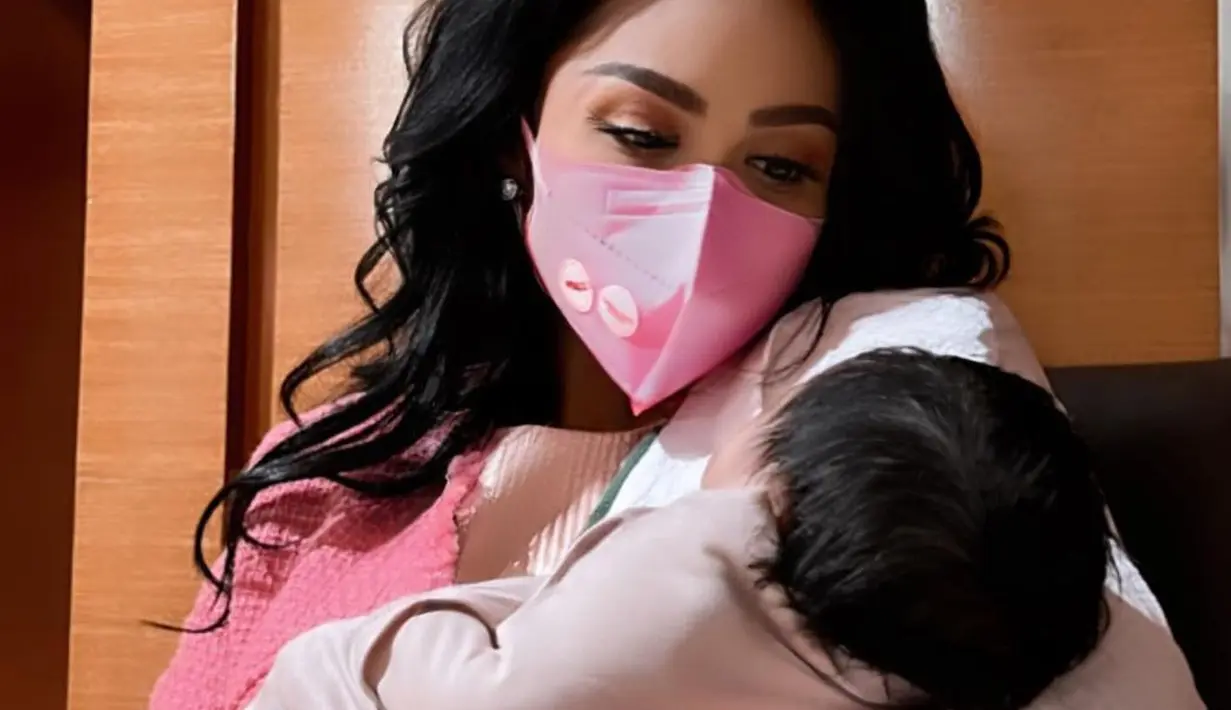 Di momen kelahiran putri pertama Aurel, Krisdayanti juga sempat membagikan potret bahagianya menggendong sang cucu. Dalam outfit berwarna merah muda dan rambut hitamnya yang dibiarkan tergerai, ia tampil menggendong sang cucu, walau dengan mengenakan masker. Foto: Instagram.